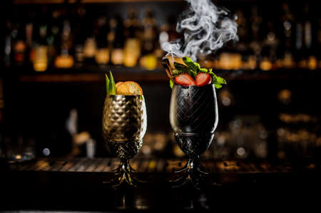 Two glasses of fresh summer cocktails decorated with fruit and fume on the bar counterの写真素材