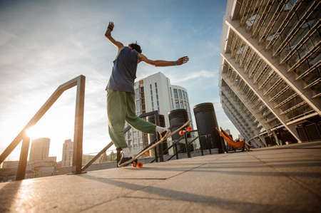 Back view of young active man jumping on skateboard against the background of city buildings on summer dayの写真素材