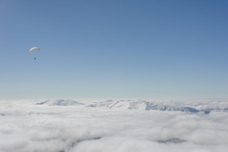 snowboarders fly on a paraglider above the clouds against the blue sky and snow mountains