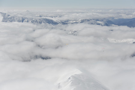 Paragliding in a cloudy blue sky over the mountains covered with white snow and iceの写真素材