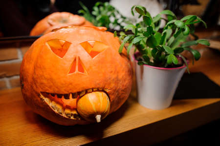 Halloween horror ball orange pumkin with the light inside with the small pumkin in the mouth near the green plant in the white potの写真素材