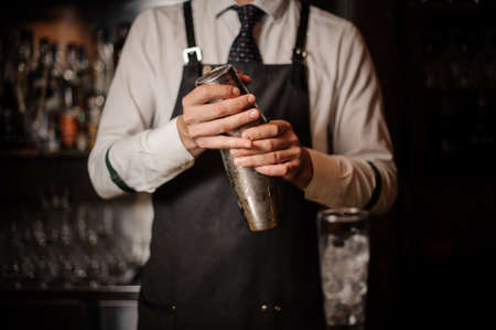 Professional bartender holding a steel cocktail shaker ready to prepare a fresh cocktail at the bar counterの写真素材
