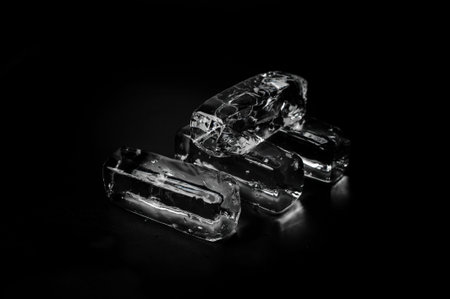 Four rectangular clear transparent ice blocks isolated on the black background shining under the...