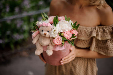 Woman holding a box filled with pink and white flowers decorated with a cute toyの写真素材