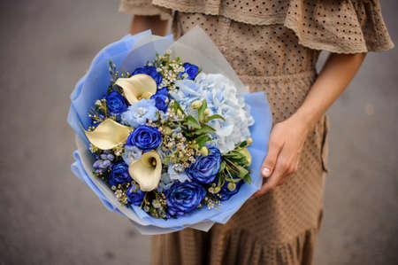 Girl in beige dress holding a romantic bouquet of flowers in tender and soft blue tonesの写真素材