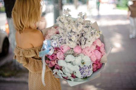 Back view of blonde woman holding a big bouquet of various colorful flowers like peonies, roses etc.の写真素材