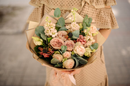 Woman in beige dress holding a nude colored bouquet of flowers wrapped in craft paperの写真素材