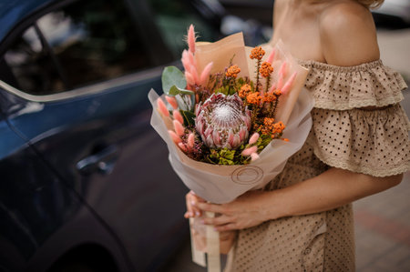 Beautiful woman in beige dress with open shoulders holding a nude colored bouquet of flowers with...
