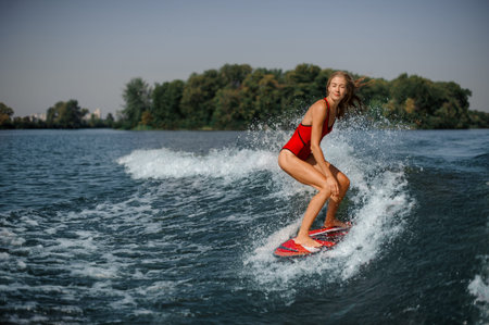 Beautiful and slim blonde woman wakesurfer riding down the blue splashing wave on a warm dayの写真素材