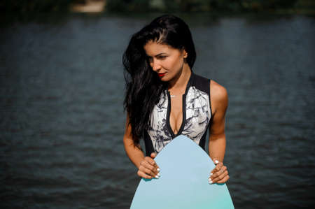 Sexy brunette woman in white swimsuit holding a wakesurf on the background of blue waterの写真素材