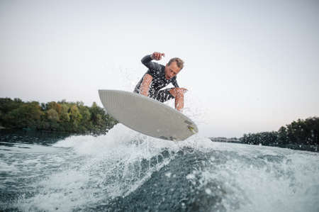 Young wakeboarder in swimsuit jumping on the blue wave against the background of clear grey skyの写真素材