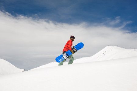 a guy in a red checked shirt and warm pants rises to the snow-covered mountain, holding a blue...
