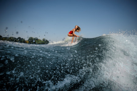 Beautiful blonde girl in the red swimsuit riding on the red wakeboard on the bending knees on the...