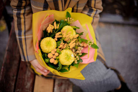 Top view of woman in plaid coat sitting on bench with a bouquet of yellow flowersの写真素材