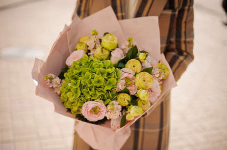 Woman holding a beautiful bouquet of flowers wrapped in craft paper on warm autumn dayの写真素材