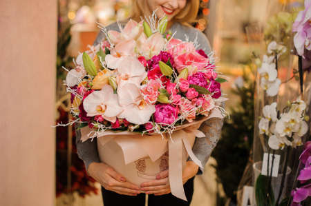 Young beautiful girl in grey shirt holding in her hands a huge box of tender pink peonies, roses and orchidsの写真素材