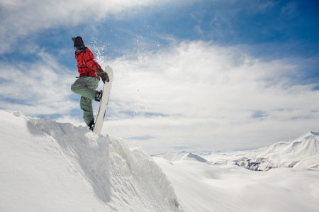 Jumping snowboarder keeping his one hand on the snowboard on the amazing blue sky background