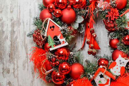 Bright Christmas Wreath decorated with red balls, feathers, cute toy houses and owl on the wooden backgroundの写真素材