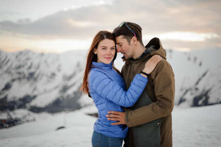 Young couple in love on the winter vacations standing on the background of high mountainsの写真素材