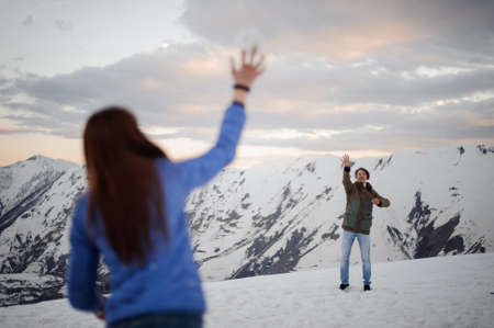Young man and woman waving their hands standing on the background of the winter mountainsの写真素材