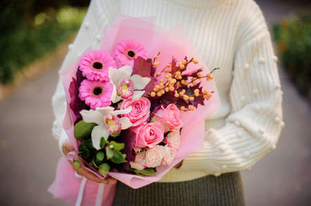Woman in the white sweather holding in her hands a huge bouquet of pink and white tender flowersの写真素材