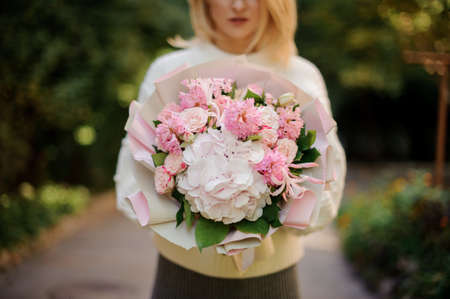 Woman in the white sweather holding in her hands a huge bouquet of tender pink flowers decorated with green leavesの写真素材