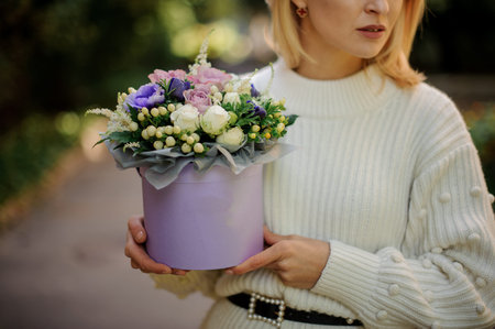 Blonde girl in the white sweather holding in her hands a box of tender white, blue and violet...