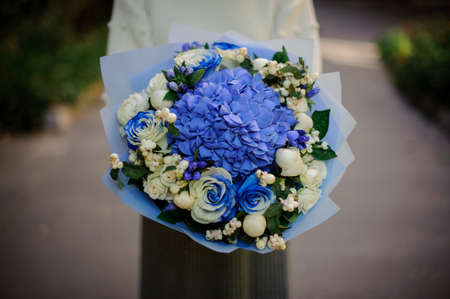 Woman in the white sweather holding in her hands bouquet of tender blue flowers in blue paperの写真素材