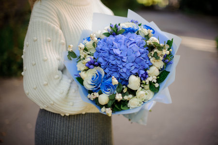 Girl in the white sweather holding in her hands bouquet of tender blue flowers in blue paperの写真素材