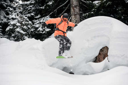 Man jumping from the mountain hill on the snowboard on the background of trees in the mountain tourist resort in Goderzi, Georgiaの写真素材