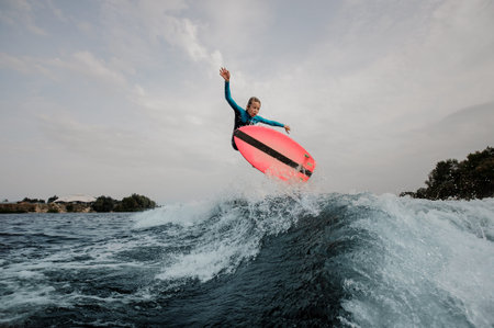 Active teenager boy jumping on the orange wakeboard having healthy summertime on the river on the...