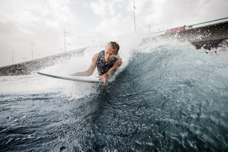 Wakesurfer lying on white board and swimming down the blue river against the cloudy sky and bridge
