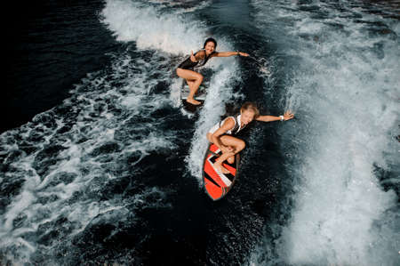 Two attractive girls in the black and white and red swimsuit riding on the wakeboardsの写真素材