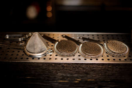 Set of professional barman tools including steel strainers on the bar counter against dark backgroundの写真素材