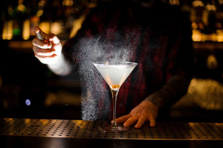 Barman spraying bitter on the elegant glass with fresh martini with olive on the bar counterの写真素材