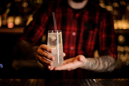 Male barman holding elegant long drink glass filled with Tom Collins cocktail against the lightsの写真素材