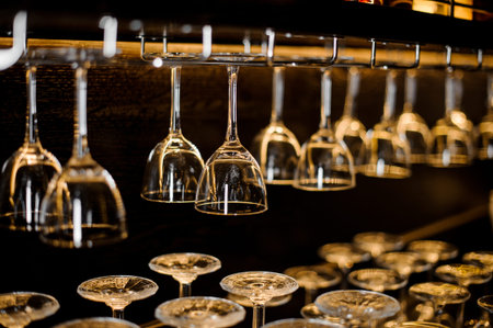 Many empty cocktail glasses standind and hanging on the bar counter on dark blurred background