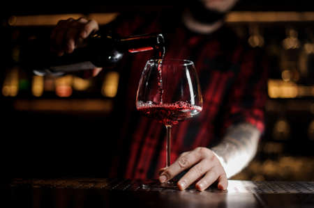 Professional bartender pourring a delicious wine from a bottle to a glassの写真素材