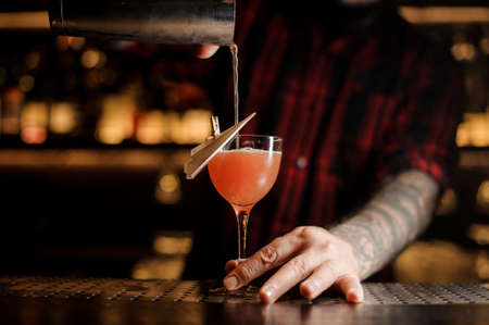 Professional bartender pourring an alcohol making cocktail in the glassの写真素材