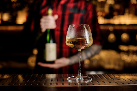Elegant white wine glass willed with tasty drink and barman with bottle of it