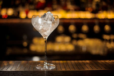 Glass of ice cubes standing on the steel bar counter on the blurred dark backgroundの写真素材