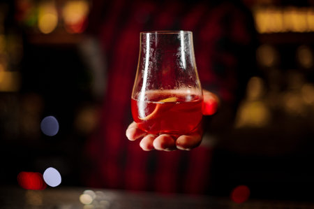 Bartender serving glass of a Sazerac cocktail decorated with orange zest on the bar counter on the...