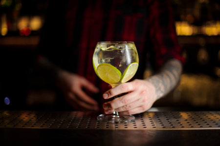 Bartender serving Gin Tonic cocktail decorated with lime slices standing on the steel bar counter on...
