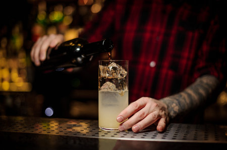 Bartender pourring a achohol from the bottle to the glass of ice cubes on the bar counter