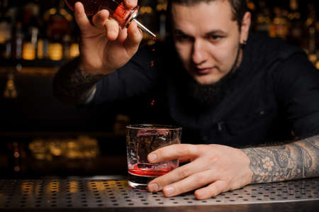 Bartender pouring red syrup into a glass with ice cube making tasty and sweet alcoholic cocktailの写真素材