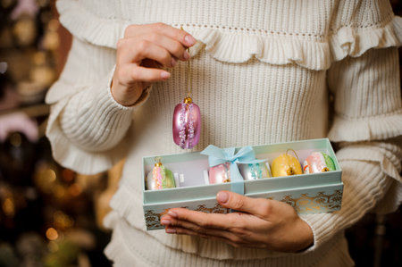 Girl holding a violet macaroon and box of many glittering toy bulbs of different colors on the blurred backgroundの写真素材