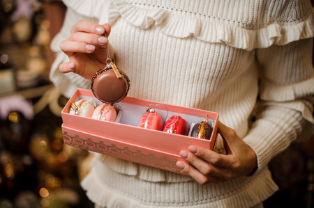 Girl holding a brown macaroon and box of many glittering toy bulbs of different colors on the...