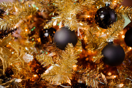New year background of golden fir tree with small black bulbs on the blurred background