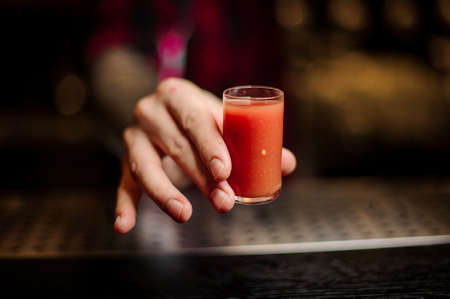 Barman hand holding a glass shot of strong tomato alcoholic drinkの写真素材