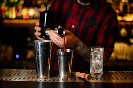 Barman pouring strong whiskey drink into a shaker